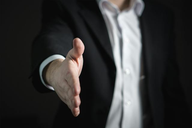 A man in a suit extends his hand out for a handshake. 