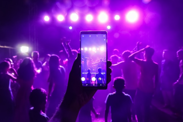 Iemand gebruikt zijn telefoon om opnames te maken van dansende mensen tijdens een concert. 