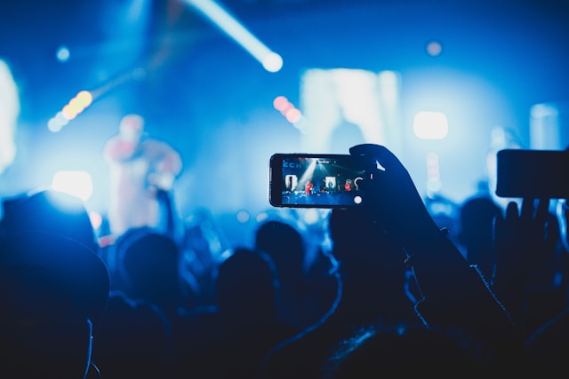 A person in a crowded concert uses their cellphone to record the performer on the stage.