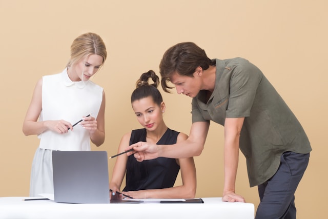 Three professionals gather around a laptop and discuss their TikTok strategy.
