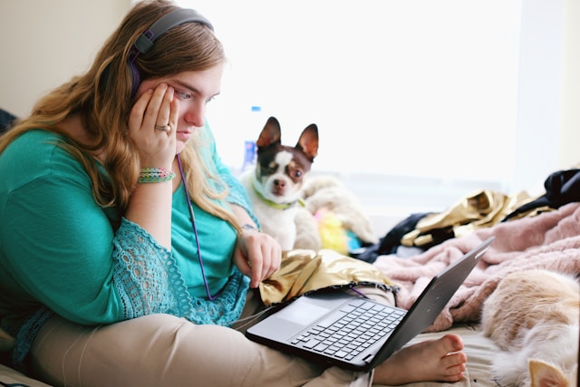 Uma mulher com fones de ouvido senta-se na cama com seu cachorro e parece perplexa enquanto navega pela sua página do TikTok.