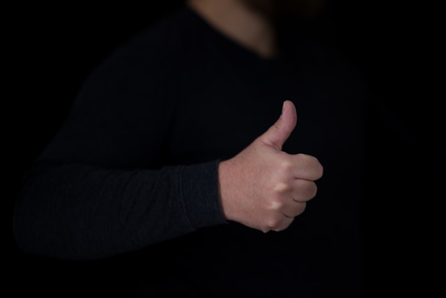 A person in a black shirt gives a thumbs up. 