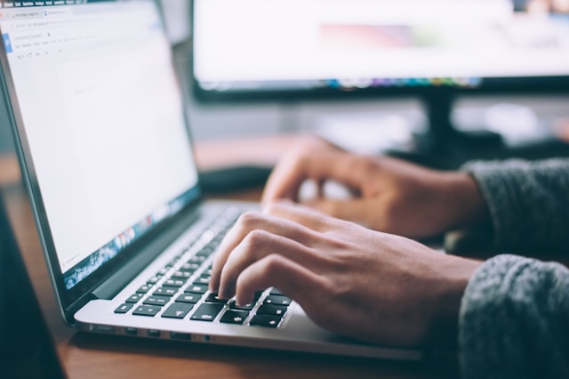 A person’s hands type on a laptop keyboard. 