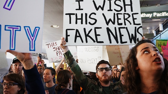 People at a protest hold up signs that say, “I wish this were fake news.”
