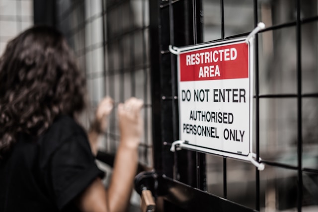 A person grabs a metal gate with a red, black, and white Restricted sign on it. 
