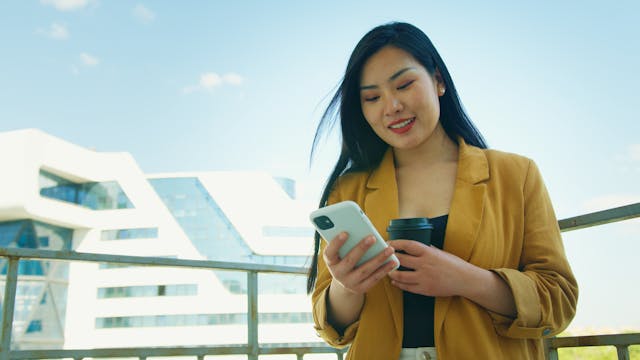 A woman scrolls on her phone while smiling.