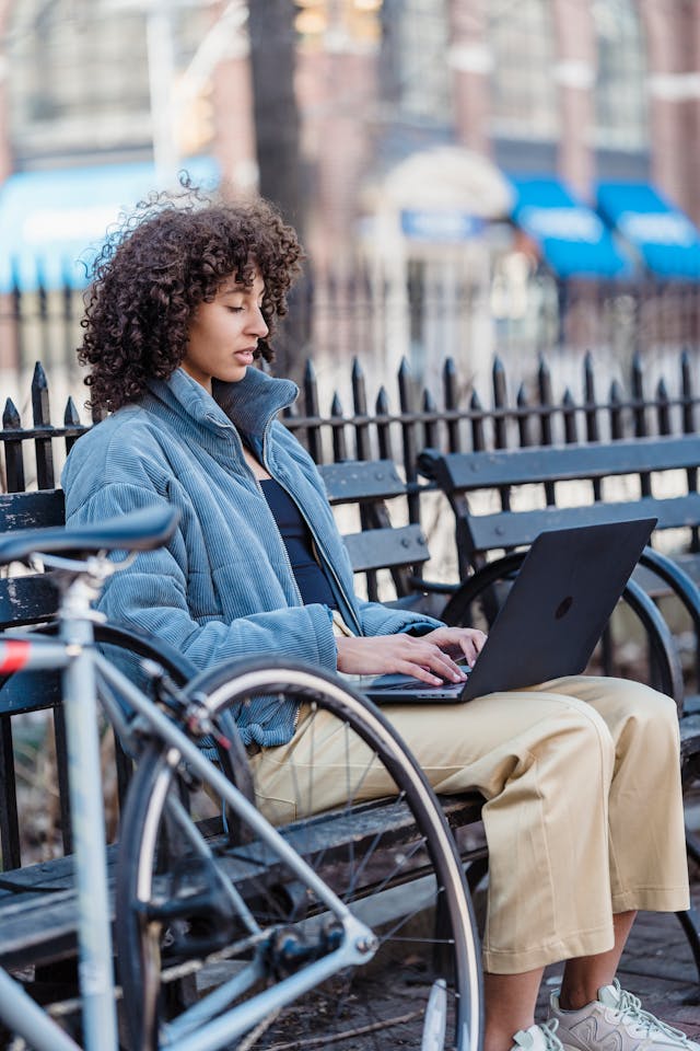 A woman on a park bench uses a laptop.
