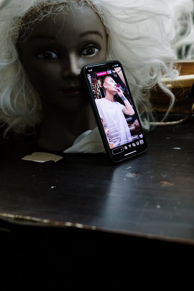 A phone showing a live stream leans on a mannequin head.