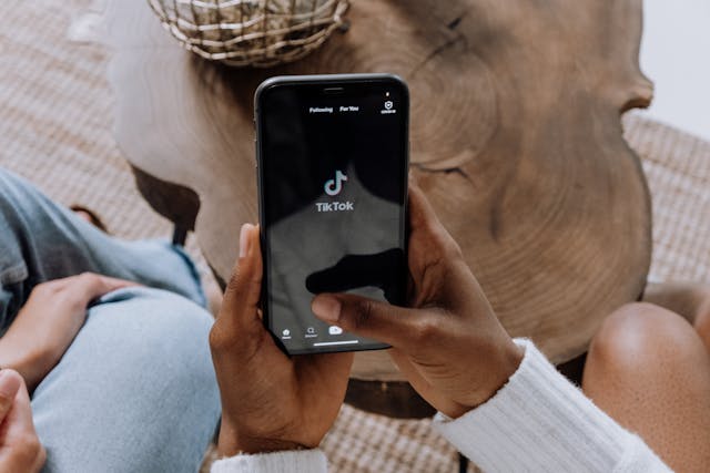 A person in front of a log holds a smartphone that displays the TikTok logo.