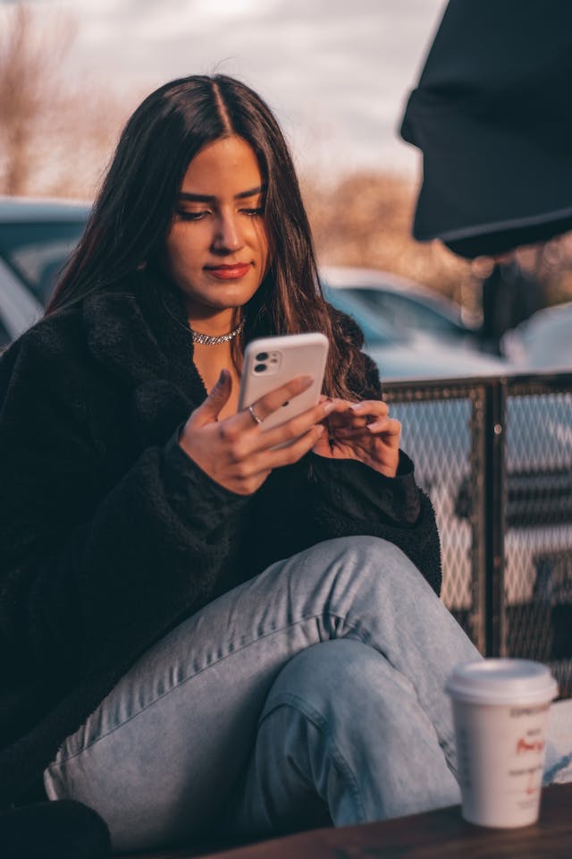 A woman holds a phone while sitting in front of a coffee cup.