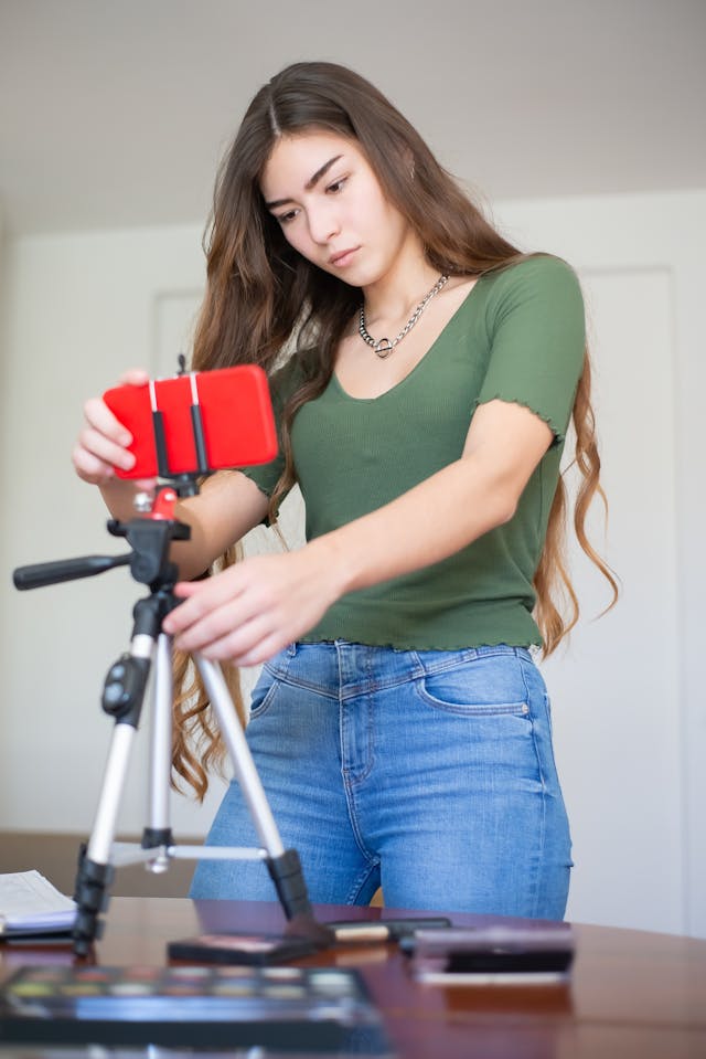 A woman sets up her phone on a tripod.
