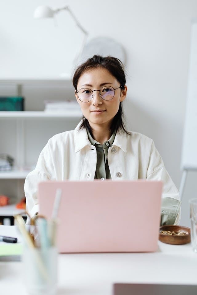 A woman sits in front of a pink laptop.