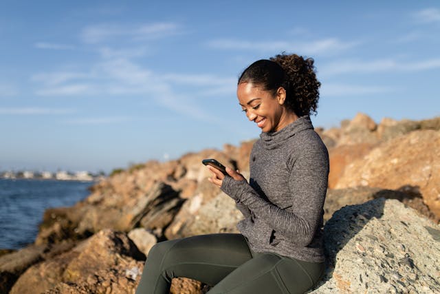 A woman looks down at her phone and smiles.
