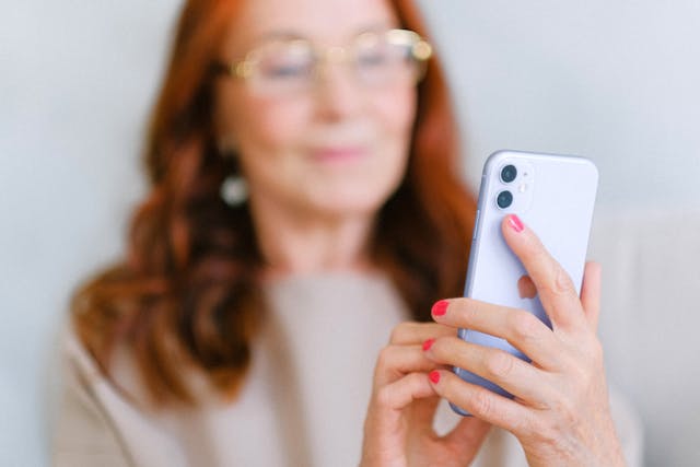 An older woman smiles while using a phone.
