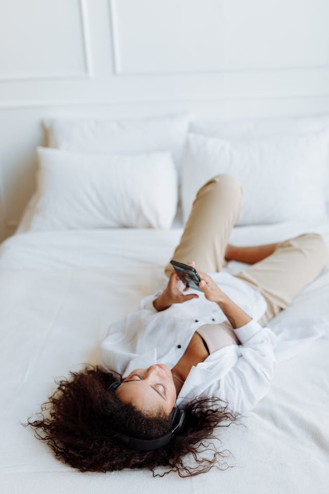 A woman lies on her back while scrolling her phone.