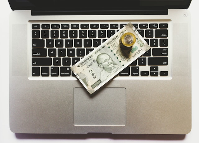 Bills and coins sit on top of a laptop keyboard. 
