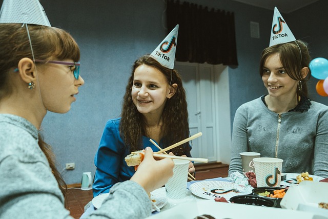 Three people celebrate a birthday while wearing pointy hats with the TikTok logo.