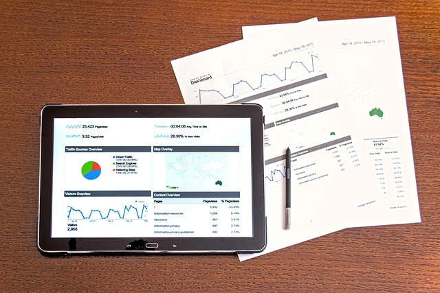 A person checks charts and analytic information on a tablet and printed copies.
