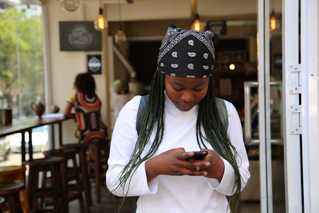 A woman in a black bandana types on her cell phone.
