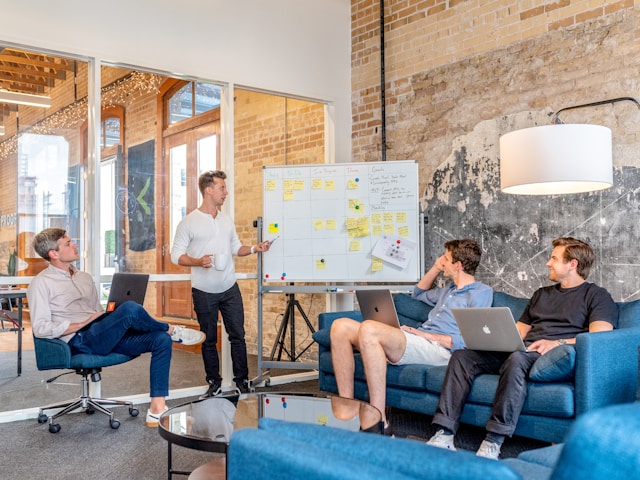 Four co-workers discuss their marketing strategy in front of a whiteboard. 
