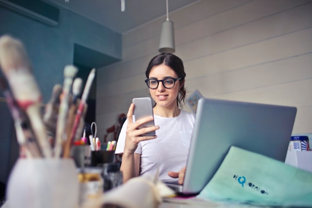 A woman in glasses smiles at her cell phone.
