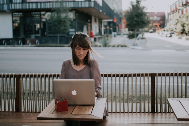 A woman types on a laptop in front of an empty street.
