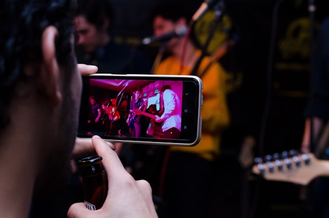 Une personne utilise un téléphone portable pour enregistrer une vidéo d'un groupe se produisant sur scène.