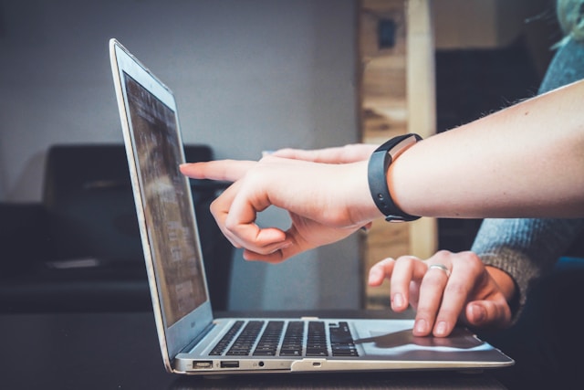 Two co-workers sit in front of a laptop and discuss their TikTok ad strategy. 
