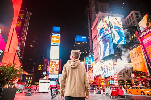 A person looks up at the towering digital billboards on a busy street at night. 
