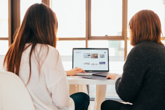 Two professionals sit in front of a laptop and discuss TikTok Ads strategies. 
