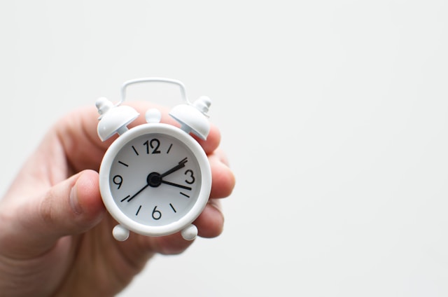 A hand holds a small, white alarm clock