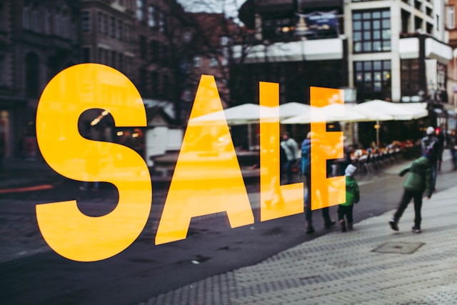 A big, yellow sale sign on the glass window of a store. 
