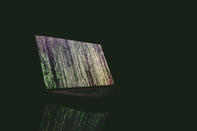 A laptop in a dark room displays lines of code on the screen.