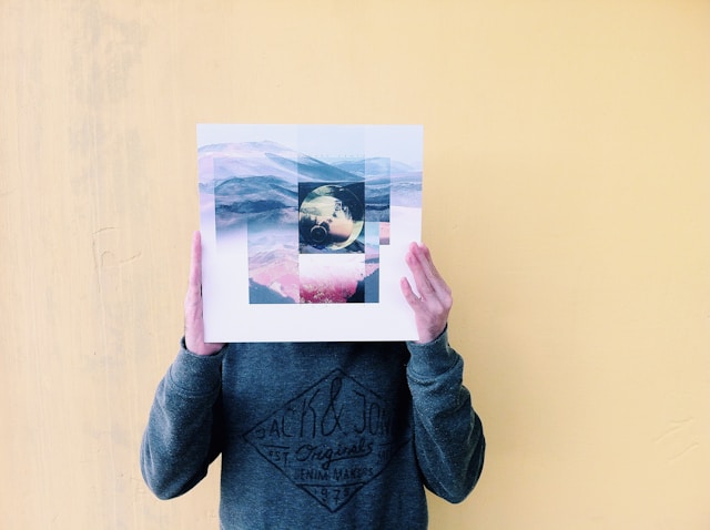 A person holds a printed collage of various landscapes in front of their face.