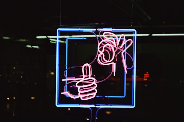 A red and blue neon signage shows one hand giving a thumbs up and another hand making the okay sign. 
