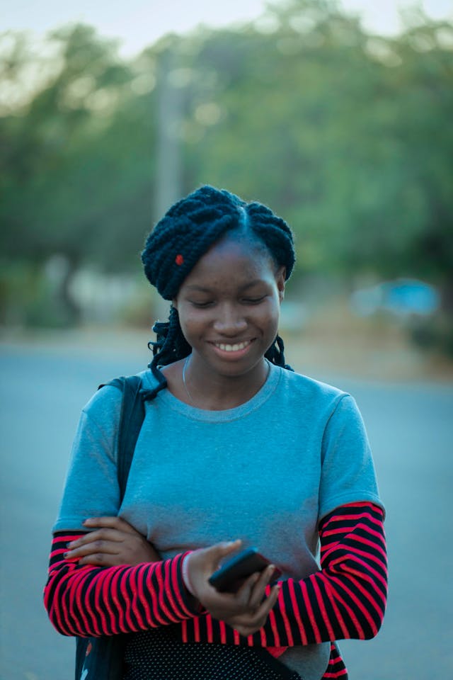 A woman looks down at her cell phone and smiles.
