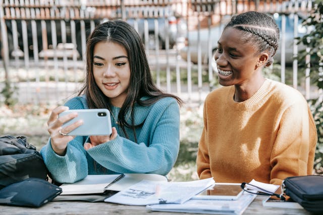 Two women smile while looking at a phone.
