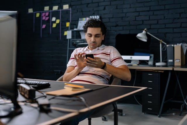 A man in a striped shirt scrolls on his phone.
