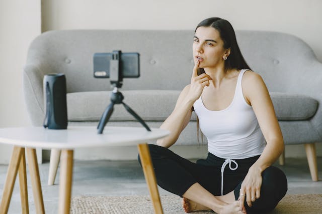 A woman stares at her phone mounted on a tripod.
