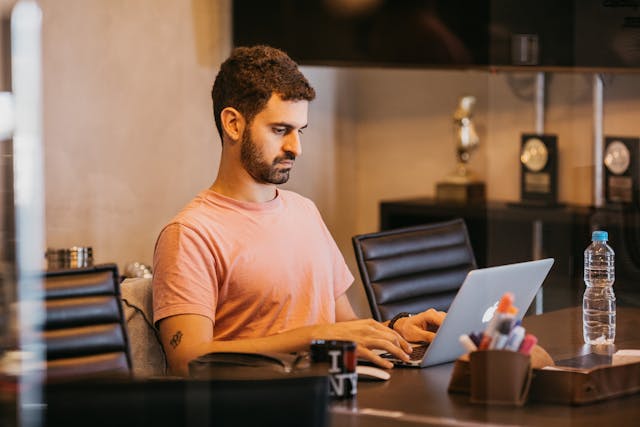 A man sitting at a desk types on his laptop.
