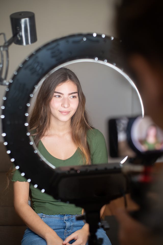 A woman sits in front of a phone and a ring light.
