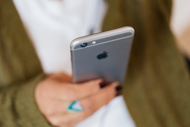 Hands with black nail polish scroll on a cell phone.
