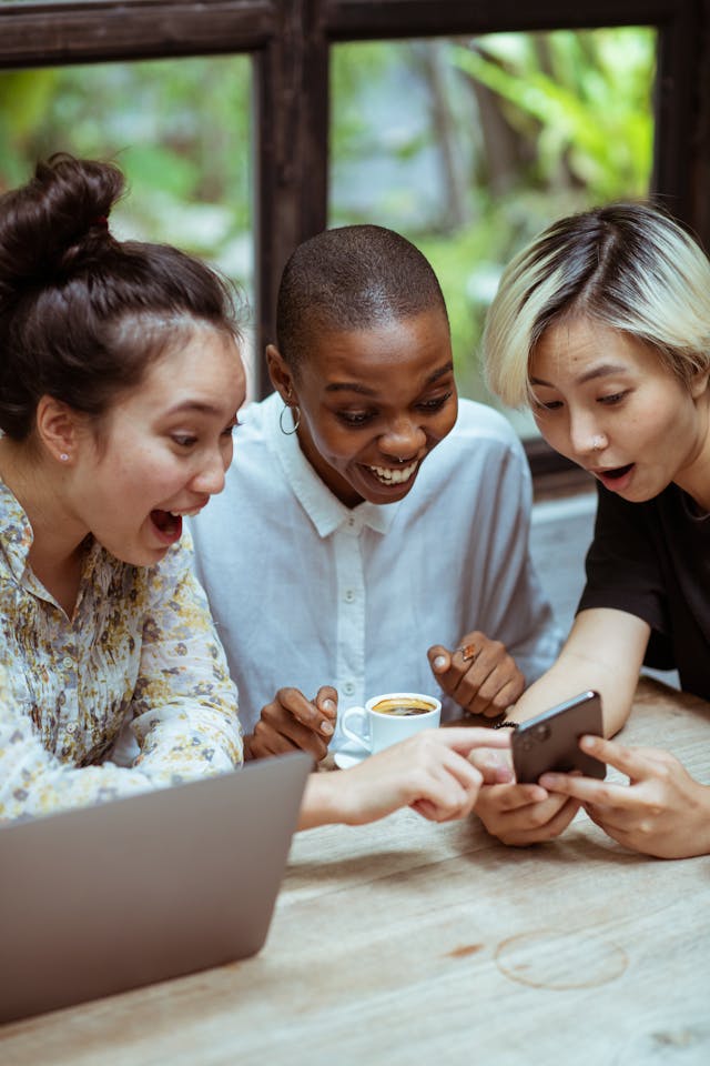 Three women look excitedly at a cell phone.