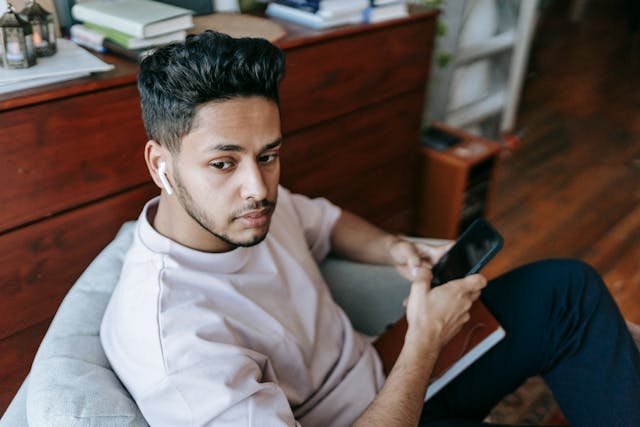 A man with earbuds holds a cell phone.
