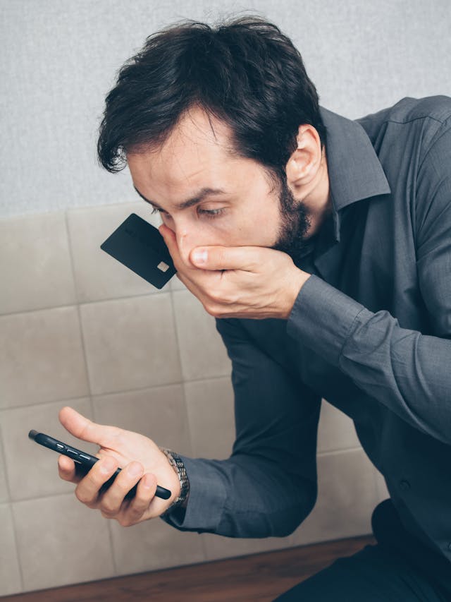 A man looks at his cell phone with one hand over his mouth.
