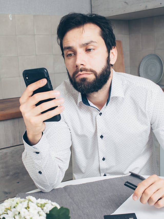 A disgruntled man looks at his phone.
