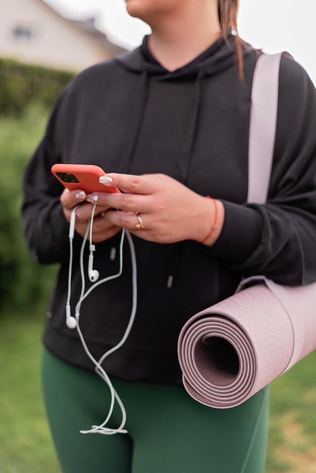 A person holds a cell phone connected to earphones.
