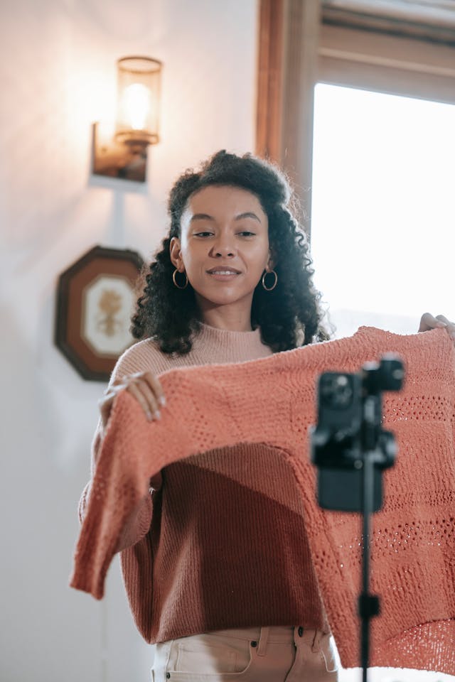 A woman shows off her sweater to a camera.
