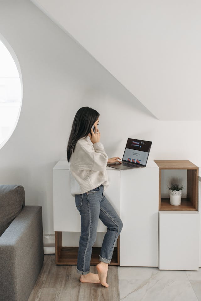 A woman stands while she uses her laptop.
