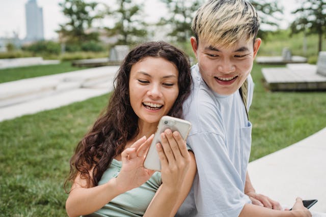 A woman laughs as she shows her phone to a man.
